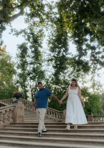 Engaged couple holding hands and walking down stone steps, captured during a romantic couples photoshoot in a lush park.