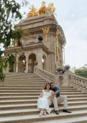 Engaged couple sitting on grand stone steps, embracing during a couples photoshoot in front of Barcelona’s Cascada Monumental