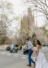 Joyful couple holding hands and crossing a street in front of Sagrada Familia during an engagement photoshoot in Barcelona.