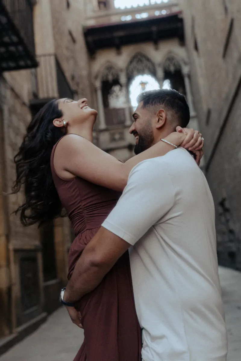 Joyful couple laughing and embracing during an engagement photoshoot in a charming old city street.