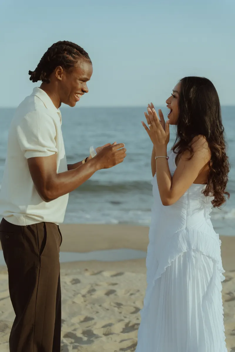 Joyful couple on the beach during a surprise proposal photoshoot, capturing genuine excitement and love.