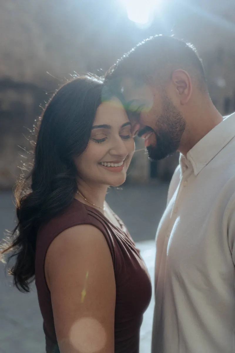 Joyful couple sharing a tender moment during an outdoor engagement photoshoot, sunlight softly illuminating their smiles.