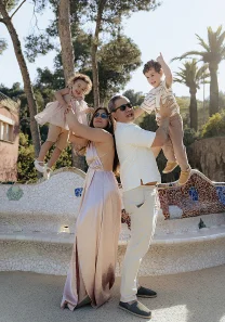 Joyful family enjoying a Vacation Portraits photoshoot, lifting their kids and laughing in sunny Park Güell, Barcelona.