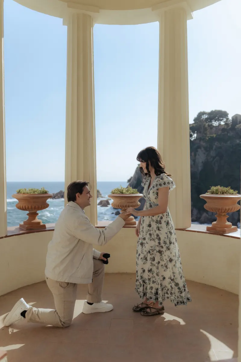 Man proposing to his partner by the sea, capturing a joyful moment during a surprise proposal photoshoot.