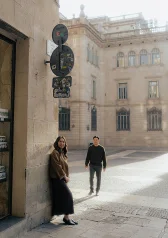 Smiling couple enjoying a Vacation Portraits photoshoot on a sunny street in a historic European city.